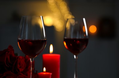 Photo of Glasses of red wine, burning candles and rose flowers against blurred lights. Romantic atmosphere