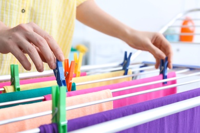 Photo of Woman hanging clean laundry on drying rack indoors, closeup