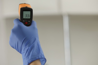 Photo of Closeup view of doctor with infrared thermometer on blurred background, space for text. Checking temperature during Covid-19 pandemic