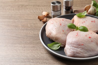 Photo of Raw chicken thighs with basil on wooden table, space for text