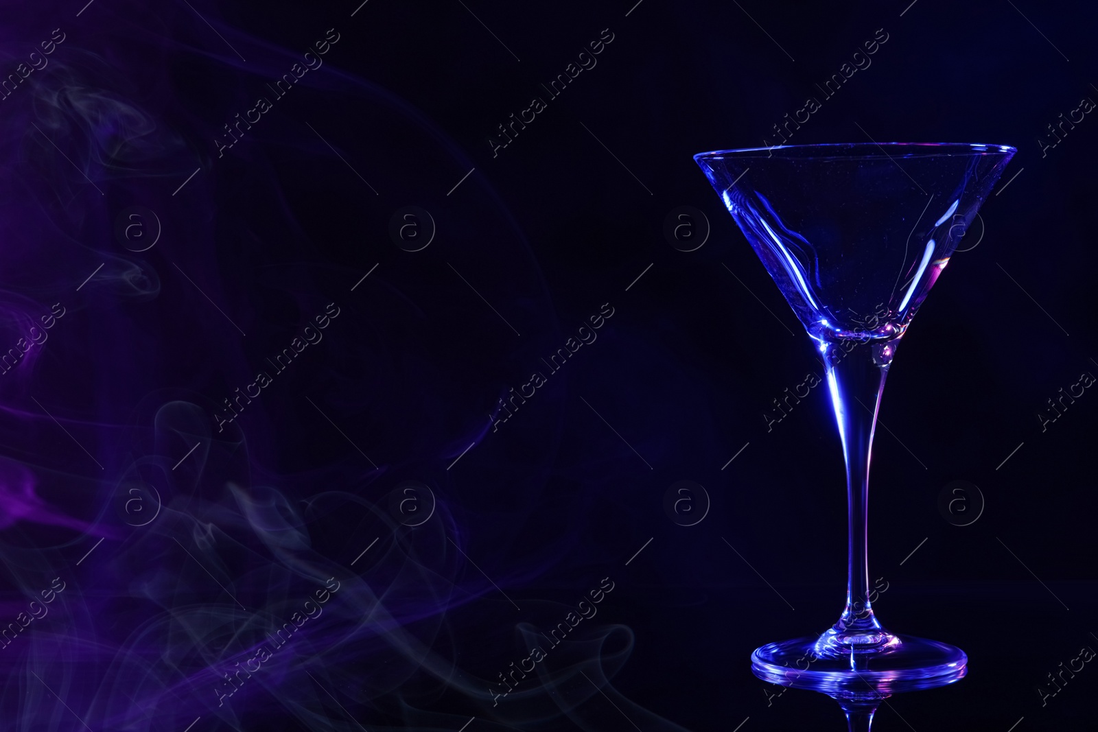 Photo of Empty clean martini glass on mirror table in neon lights, space for text