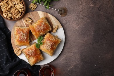 Photo of Eastern sweets. Pieces of tasty baklava, walnuts and tea on brown table, flat lay. Space for text