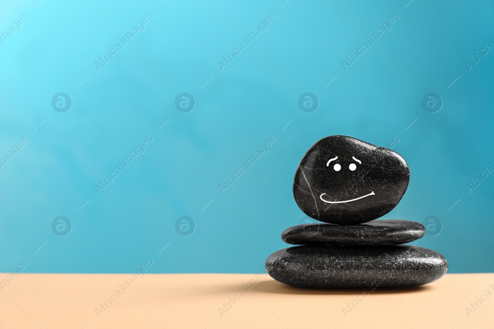 Photo of Stack of stones with drawn happy face on beige table against light blue background, space for text. Zen concept