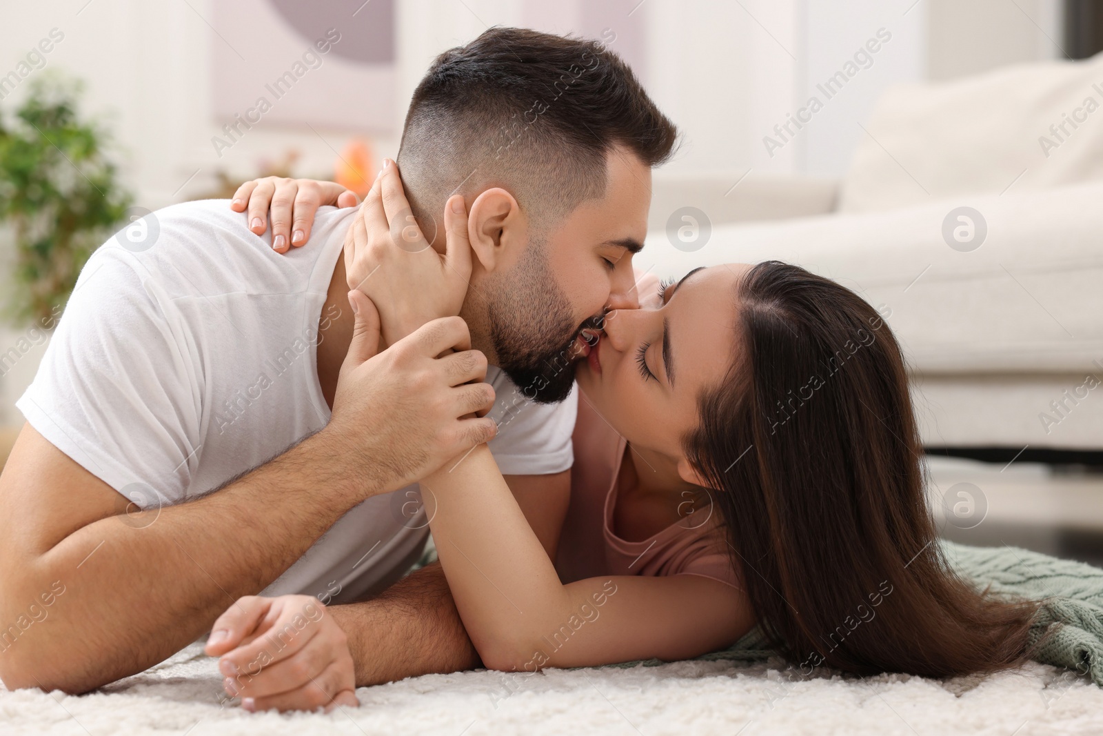 Photo of Affectionate young couple kissing on soft carpet at home