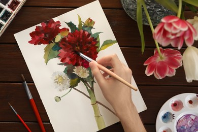 Photo of Woman painting flowers with watercolor at wooden table, top view. Creative artwork