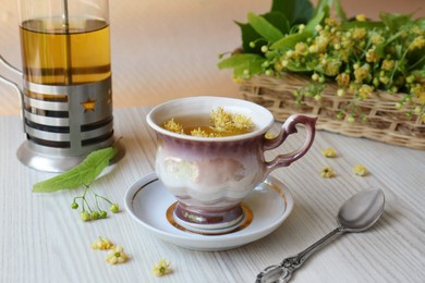 Photo of Aromatic tea with linden blossoms and spoon on white wooden table