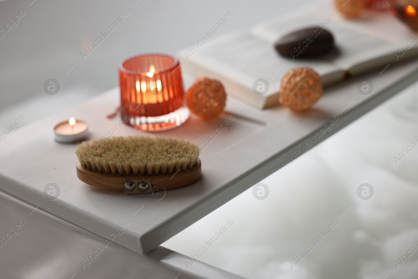 Photo of White wooden tray with burning candles and brush on bathtub