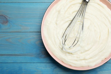 Photo of Whipping pastry cream with balloon whisk on light blue wooden table, top view. Space for text