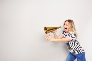 Young woman shouting into megaphone on light background. Space for text
