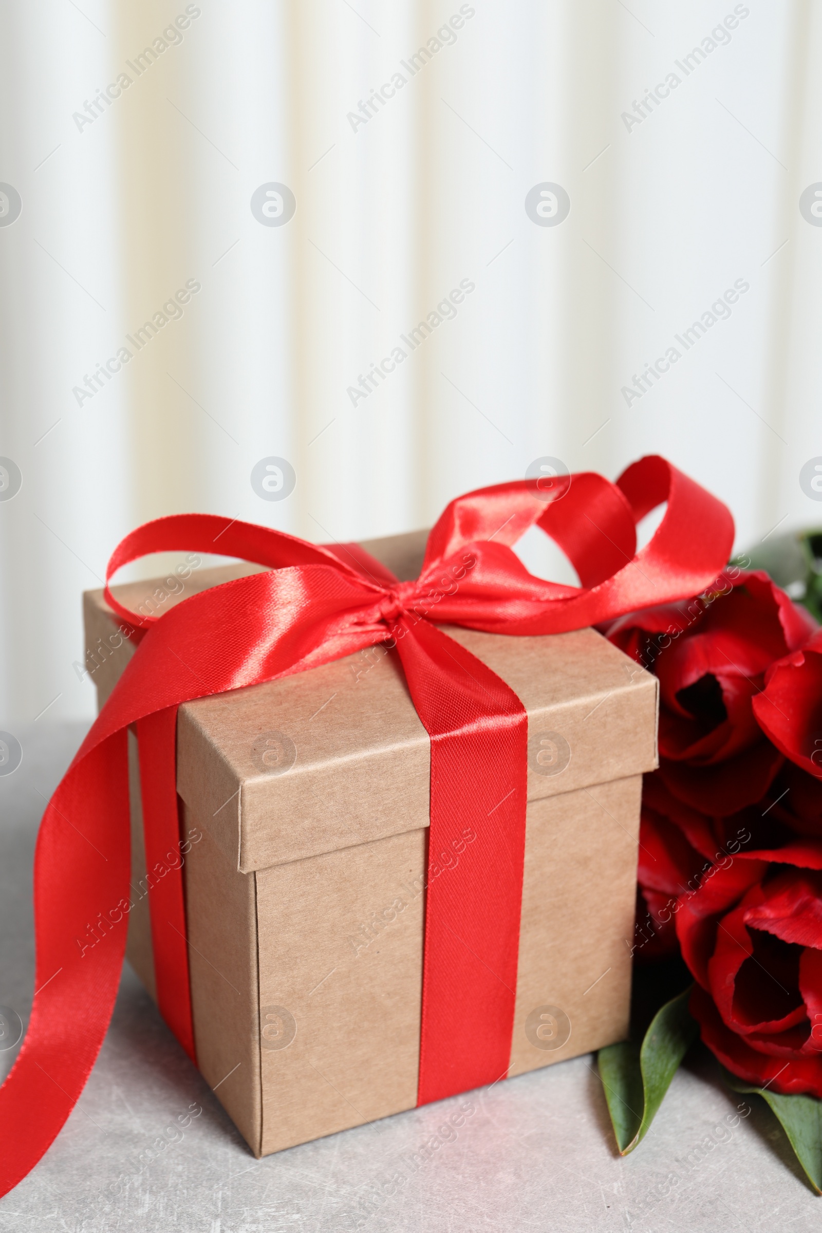 Photo of Beautiful gift box with bow and red tulip flowers on light table, closeup
