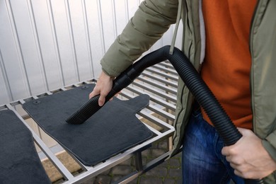 Photo of Man cleaning auto carpets with vacuum cleaner at self-service car wash, closeup