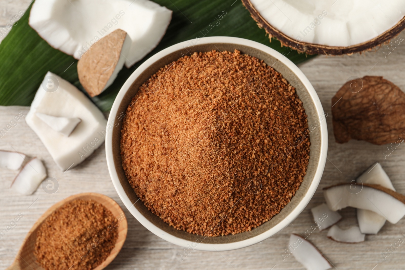 Photo of Natural coconut sugar in bowl on white wooden table, flat lay