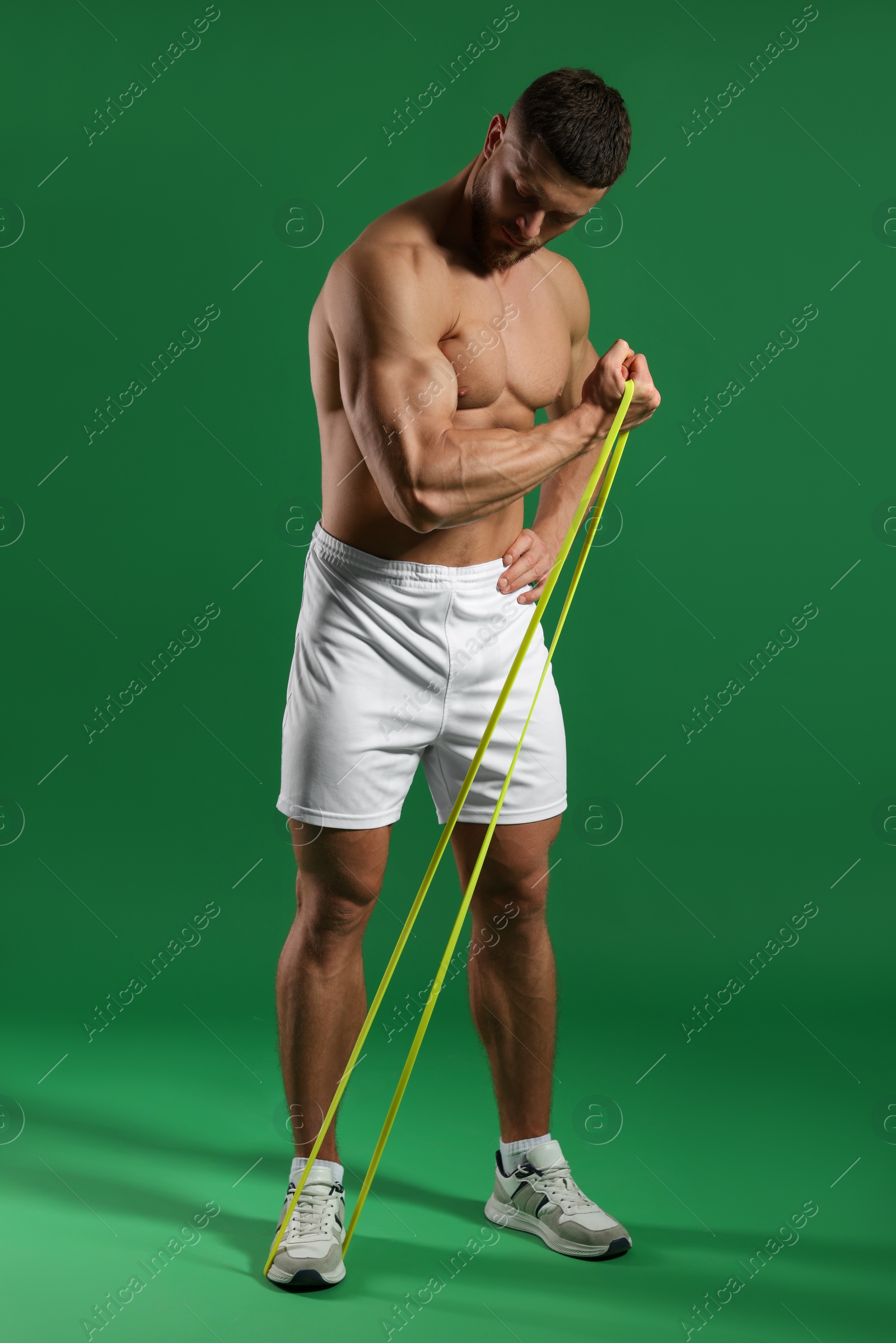 Photo of Muscular man exercising with elastic resistance band on green background