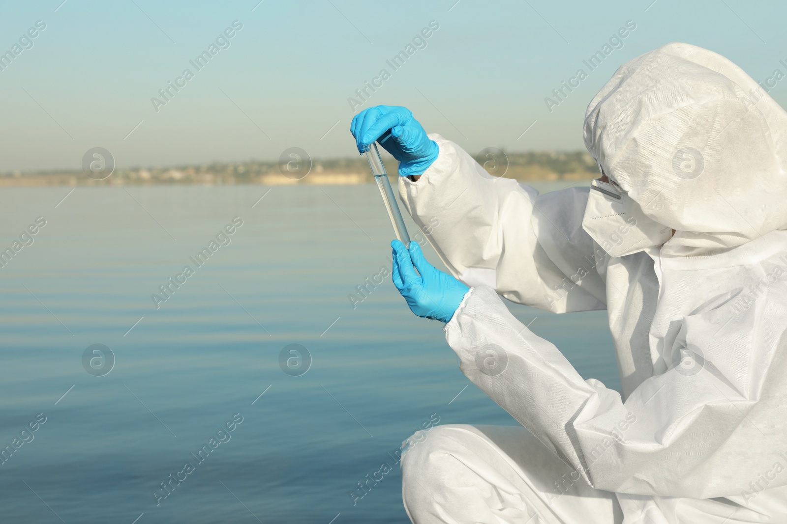 Photo of Scientist in chemical protective suit with test tube taking sample from river for analysis