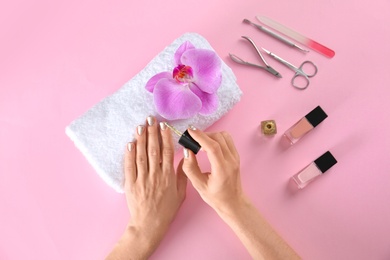 Photo of Woman applying nail polish on color background, top view