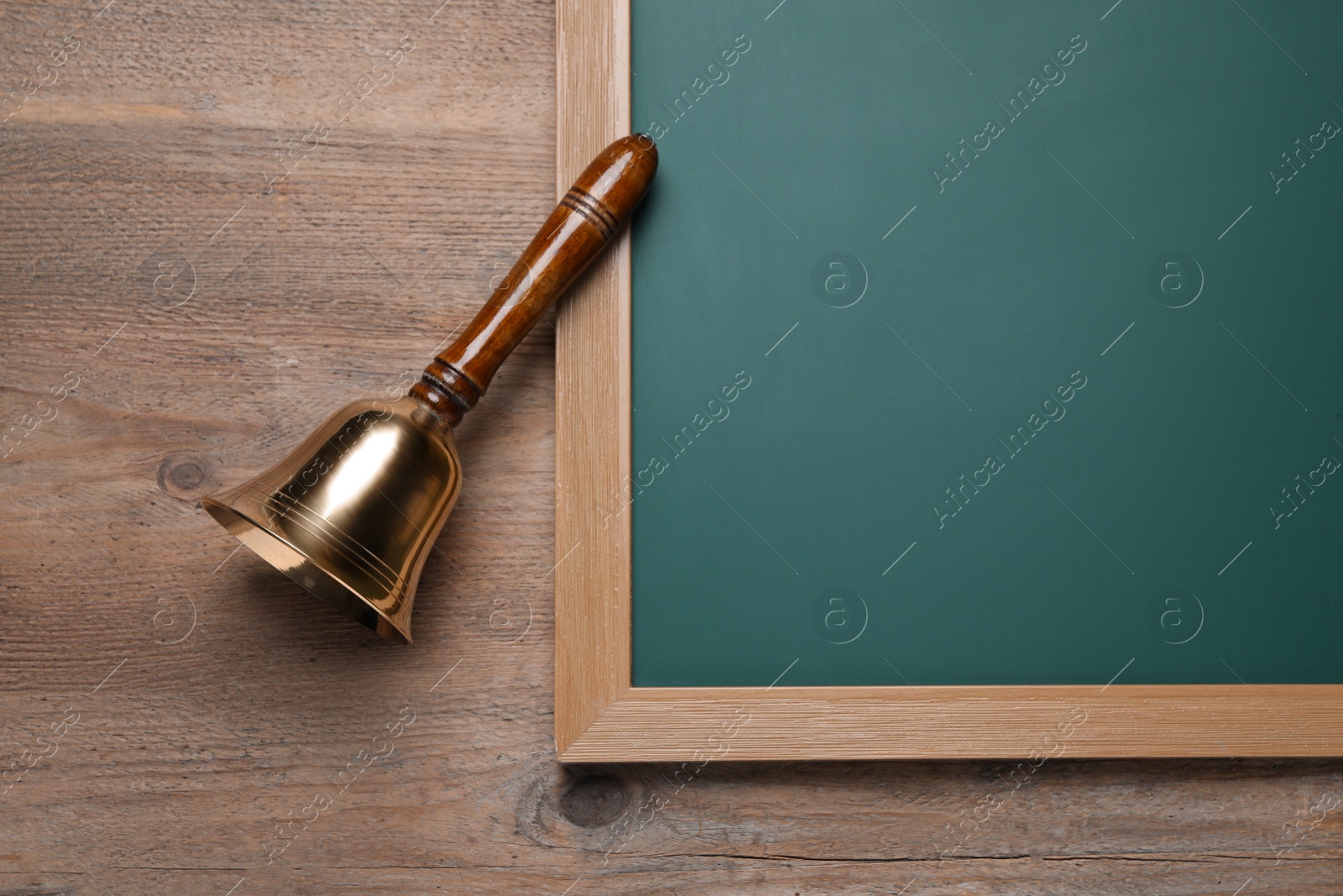 Photo of Golden bell and green chalkboard on wooden background, flat lay. School days