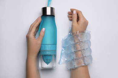 Photo of Woman with ice pack and bottle of water on white background, top view. Heat stroke treatment