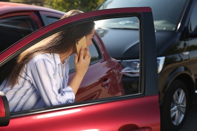 Photo of Young woman talking on phone after car accident outdoors
