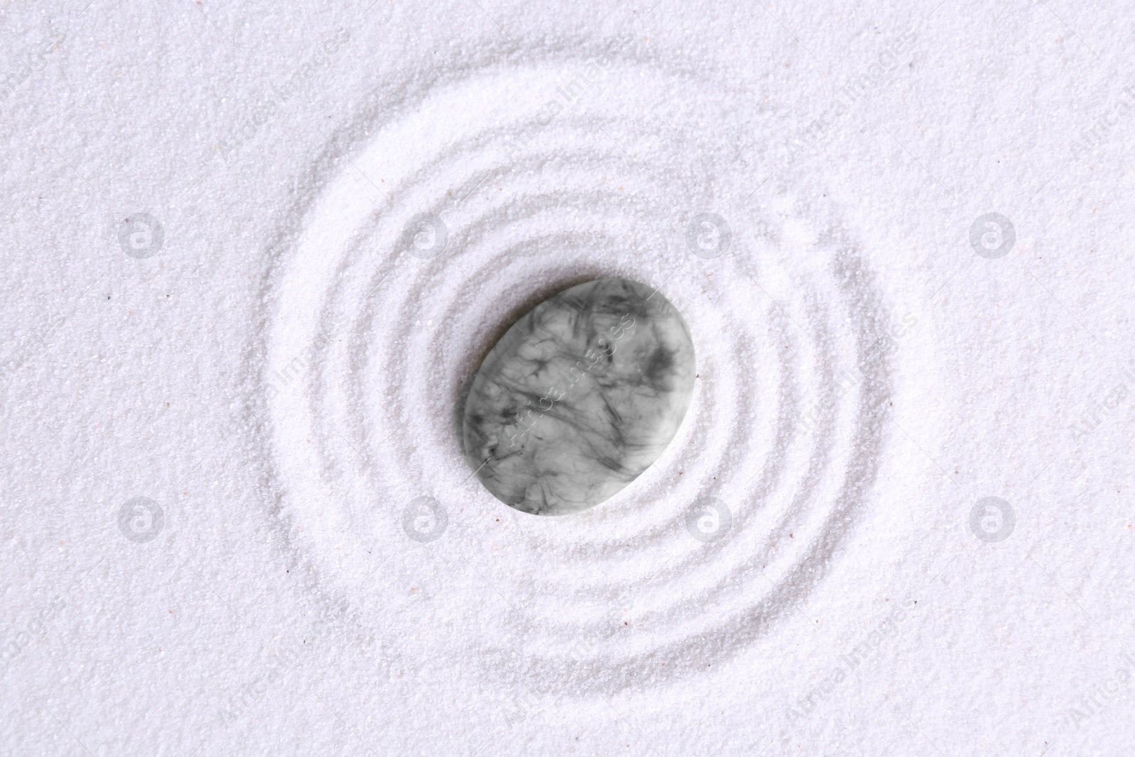 Photo of Zen garden stone on white sand with pattern, top view