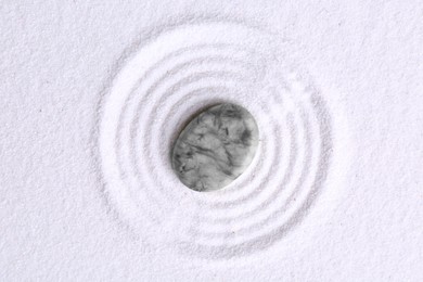 Photo of Zen garden stone on white sand with pattern, top view