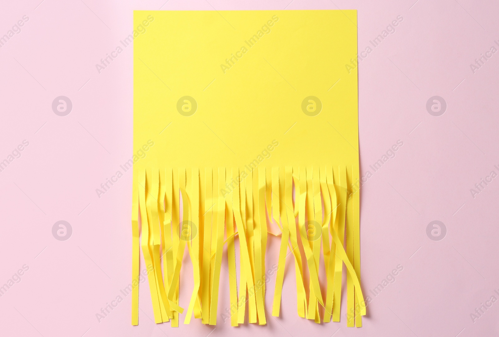Photo of Half shredded sheet of yellow paper on pink background, top view