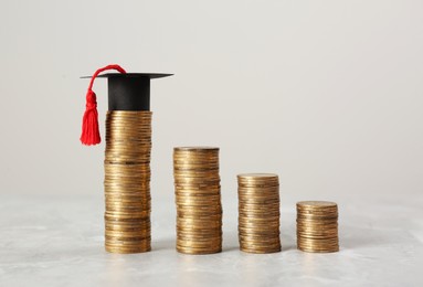 Photo of Scholarship concept. Graduation cap and stacked coins on light grey table