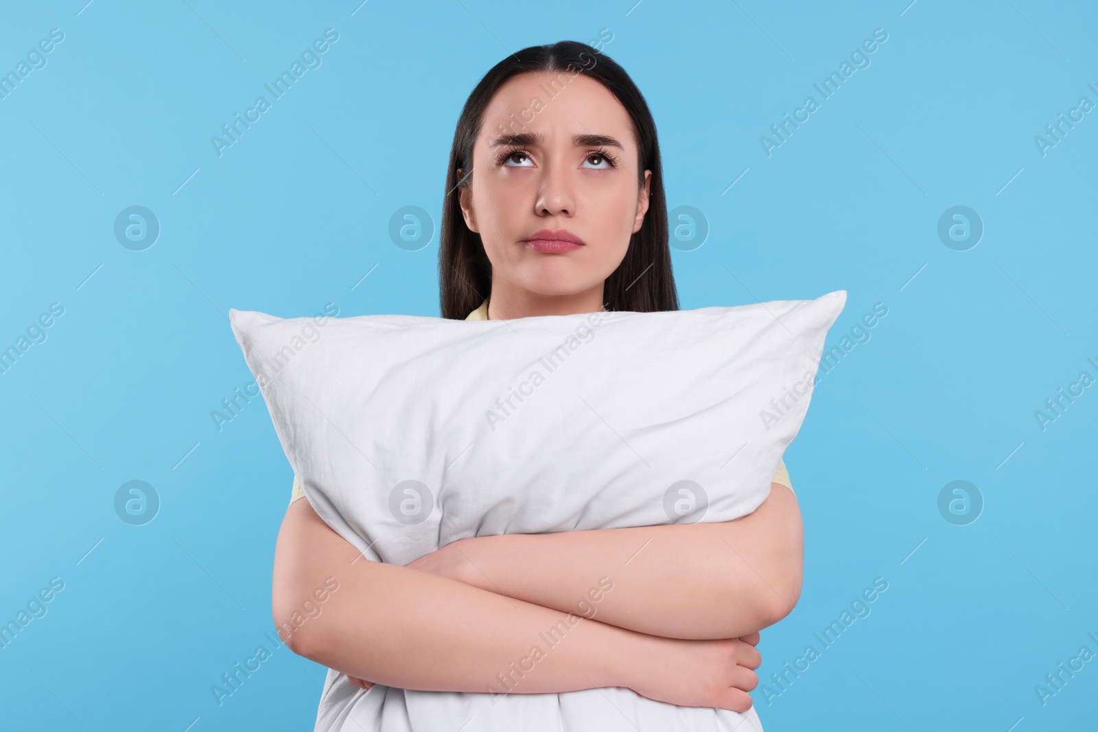 Photo of Tired young woman with pillow on light blue background. Insomnia problem