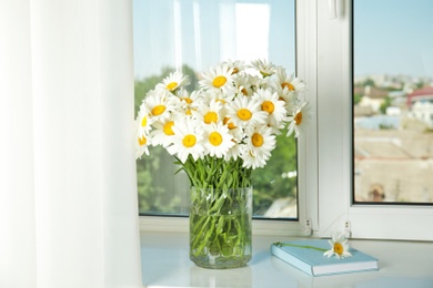 Photo of Vase with beautiful chamomile flowers on windowsill