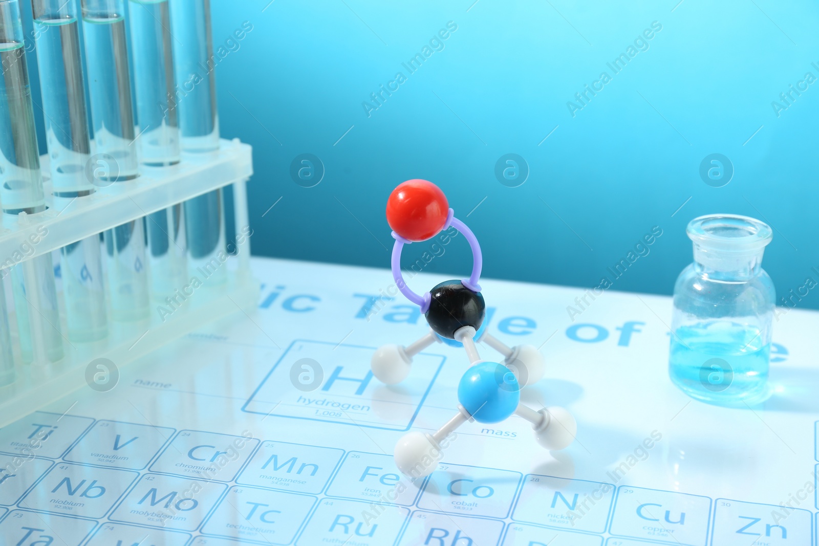 Photo of Molecular model and laboratory glassware on periodic table against light blue background