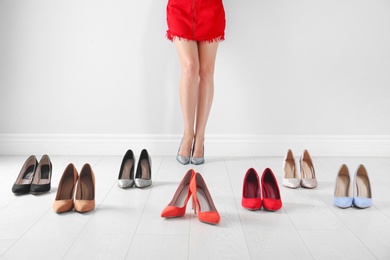 Photo of Woman trying on different high heel shoes near light wall, closeup