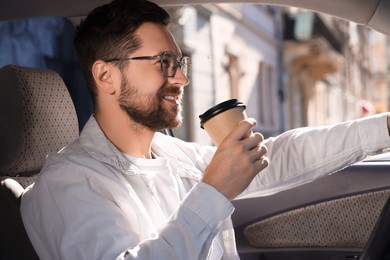 Photo of Coffee to go. Happy man with paper cup of drink in car