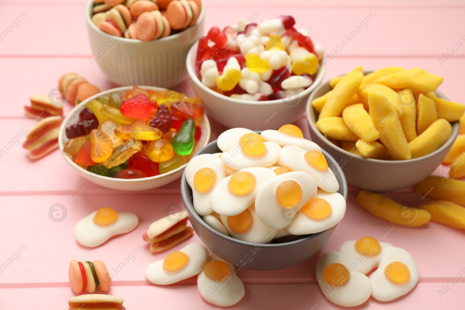 Photo of Many different delicious gummy candies on pink wooden table