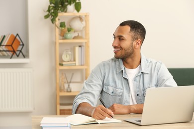 Smiling African American man near laptop at wooden table in room