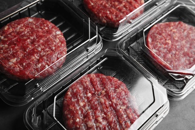 Plastic containers with raw meat cutlets for burger on table, closeup