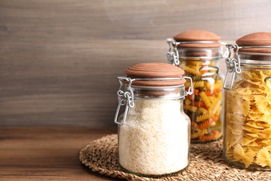 Photo of Glass jars with rice and different types of pasta on wooden table. Space for text