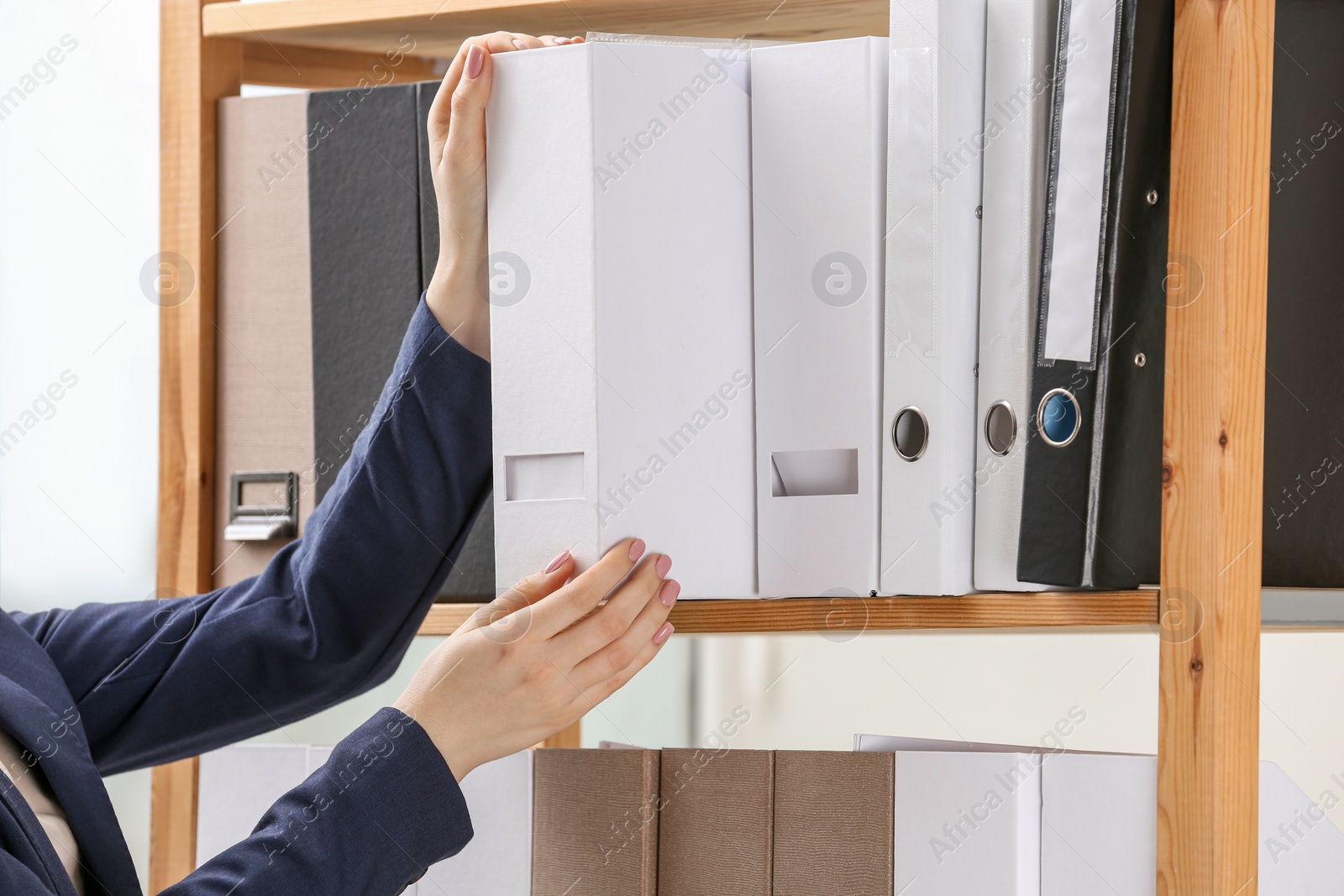 Photo of Woman taking folder with documents from shelf in office, closeup