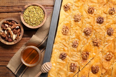 Photo of Delicious baklava with walnuts in baking pan, honey and nuts on wooden table, flat lay
