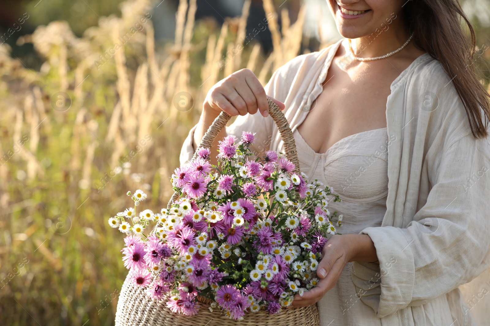 Photo of Woman holding wicker basket with beautiful wild flowers outdoors, closeup. Space for text