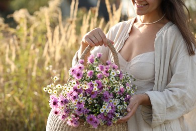 Photo of Woman holding wicker basket with beautiful wild flowers outdoors, closeup. Space for text