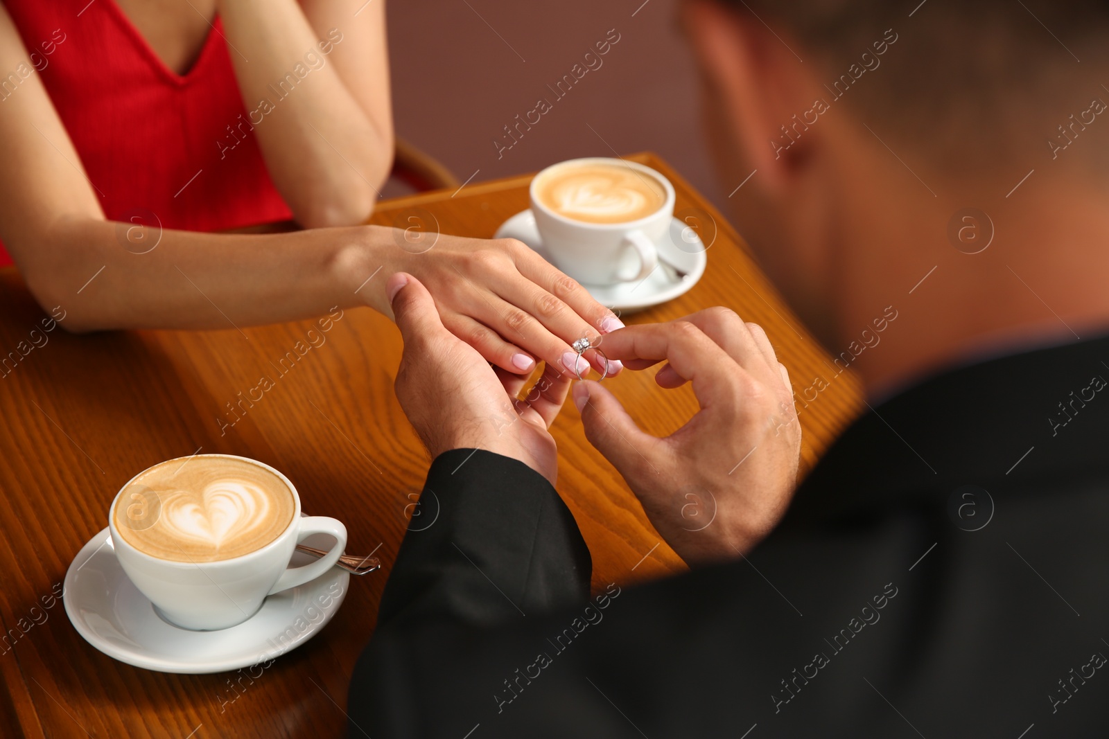 Photo of Man putting engagement ring on his girlfriend's finger in cafe, closeup