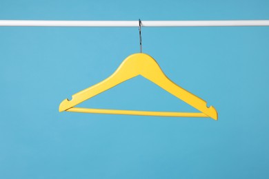 Photo of Yellow clothes hanger on metal rail against light blue background