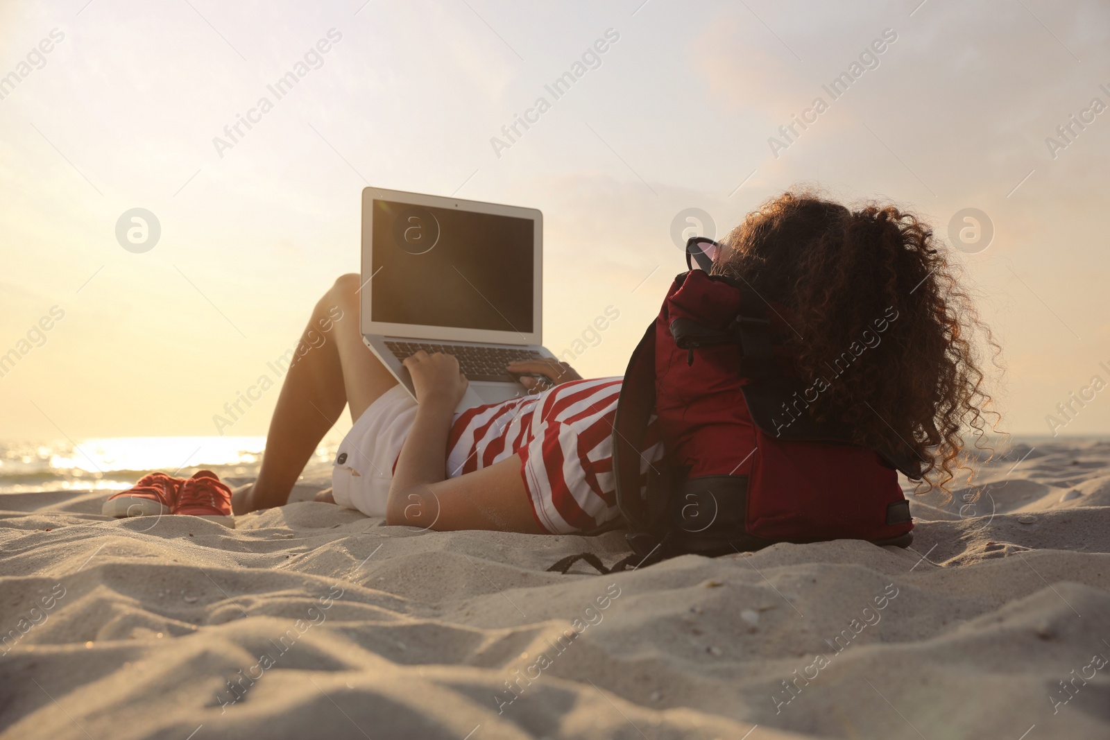 Photo of African American woman working on laptop at beach