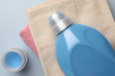 Photo of Bottle of fabric softener and stacked clean clothes on light blue background, flat lay