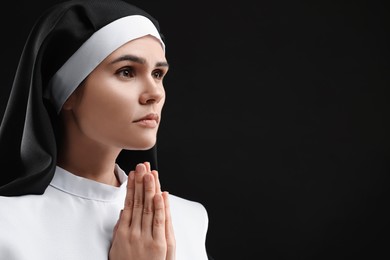 Photo of Nun with clasped hands praying to God on black background. Space for text