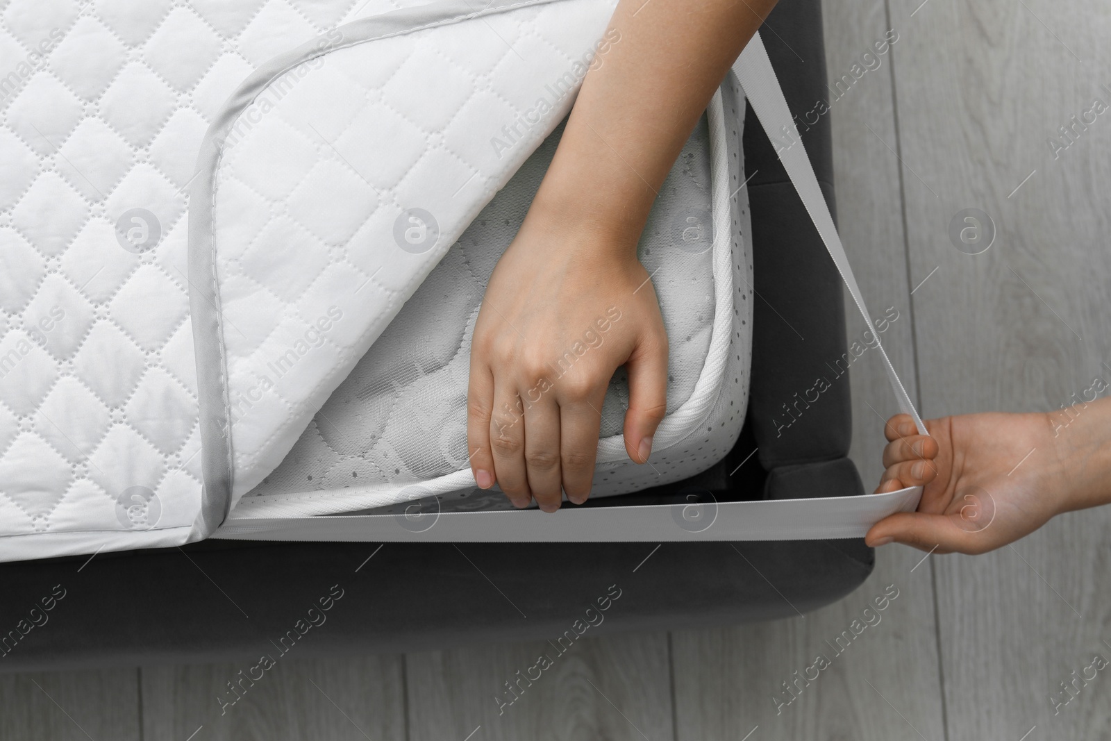 Photo of Woman putting protector on mattress indoors, top view