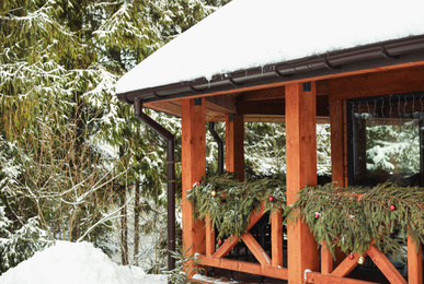 Photo of Wooden terrace decorated with fir garland near forest. Winter vacation
