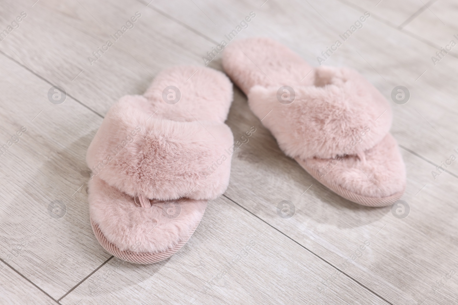 Photo of Pink soft slippers on light wooden floor at home, closeup