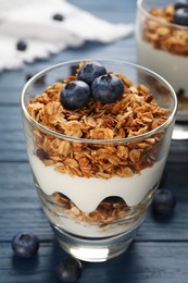 Glass of tasty yogurt with muesli and blueberries on blue wooden table