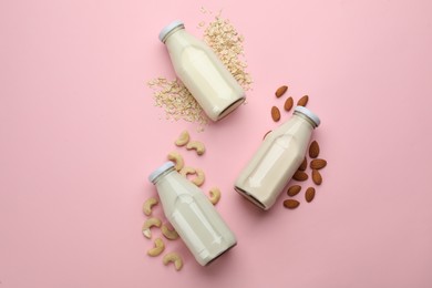 Photo of Different vegan milks, oat flakes and nuts on pink background, flat lay