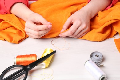 Photo of Woman sewing cloth with needle at light wooden table, closeup